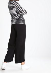 Pantalon noir à jambes larges associé à un pull à rayures noires et blanches. Le pull présente une finition en tricot texturé. Des baskets blanches complètent la tenue.