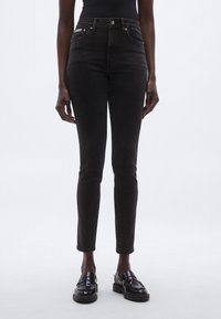 Vaqueros de mezclilla negros de cintura alta con un ajuste ceñido, cierre de botones y bolsillos delanteros. Combinados con mocasines negros, que muestran un diseño elegante.