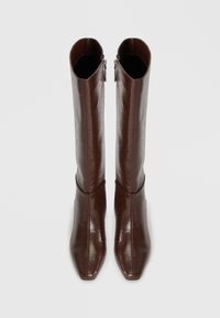 Paire de bottes hautes en cuir marron texturé avec des pointes pointues et des fermetures éclair latérales, vues de dessus sur un fond uni.