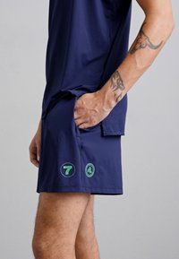 Marine treningsshorts laget av lett materiale, med sidelomme, grønne logoer på kanten, og en avslappet passform.