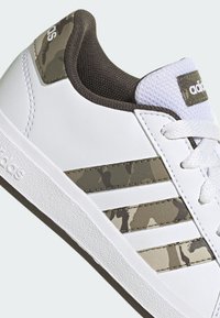 Sneaker bianco con accenti a motivo camouflage sulle tre strisce, suola in gomma testurizzata e colletto imbottito verde oliva.