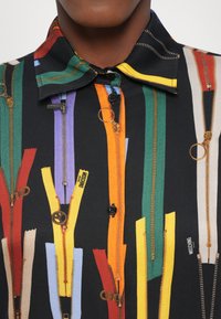 Korte mouw shirt met een zwarte achtergrond en meerkleurige ritsafdrukken in groen, oranje, paars en geel, met gouden accenten.