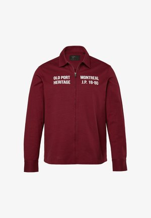 Bordeaux zip-jakke med spidse krave, lange ærmer og hvidt trykt tekst: "OLD PORT HERITAGE" og "MONTREAL J.P. 18-80." Blødt stof.
