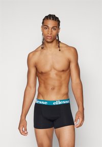 Svarta boxerkalsonger med en tealfärgad midjeresår som har "ellesse" i vita bokstäver. Slätt tyg och åtsittande design som framhäver en modern silhuett.