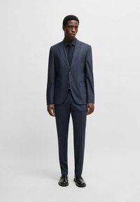Completo blu navy su misura con un tessuto testurizzato, caratterizzato da un giacca monopetto, colletto a soffietto e pantaloni slim-fit, abbinato a scarpe nere.