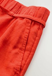Roter Stoff mit einer strukturierten, leicht zerknitterten Oberfläche. Der Bund verfügt über ein elastisches Band und einen gebundenen Stoffakzent.