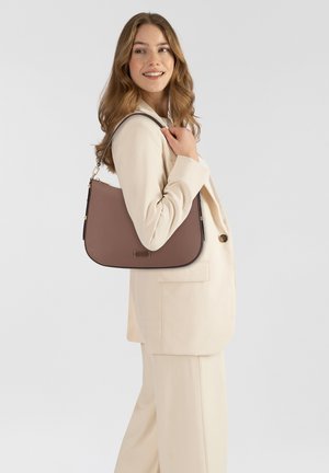 Brown leather shoulder bag with a curved shape, gold hardware, and a textured finish. Worn on the shoulder against a light-colored outfit.