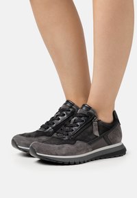 Schwarze Wildledersneaker mit strukturierten Akzenten, ausgestattet mit einer Schnürfront, seitlichem Reißverschluss und grauer Gummisohle. Niedrig geschnittenes Design.