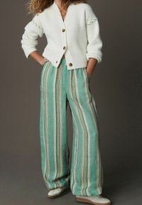 Cardigan blanc côtelé avec trois boutons, associé à un pantalon large en lin vert à rayures, présentant des rayures verticales marron et beige.