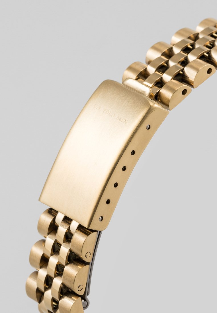 Orologio in metallo dorato con design a bracciale a maglie, caratterizzato da una cassa lucida e un logo inciso. Texture liscia e lucida con chiusura regolabile.