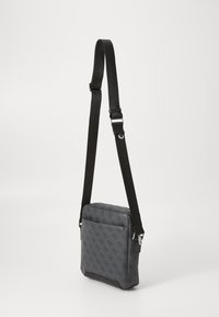 Bolso cruzado sintético gris con correa negra ajustable, cierre de cremallera, bolsillo delantero y patrón de logo en relieve. Textura suave y forma rectangular.