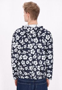 Lätt marina blå jacka med ett blommigt vitt mönster, som har en huva och långa ärmar. Bakvy visar elastisk nederkant och muddar.