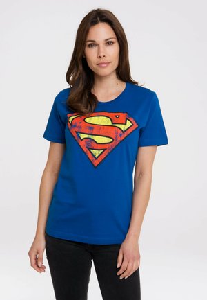 Blue cotton t-shirt featuring a large, colorful Superman logo in red and yellow. Short sleeves and round neckline, with a smooth texture.