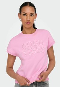 Lichtroze sweatshirt met korte mouwen, voorzien van de witte tekst "GOOD VIBES". Ribbelhals en -zoom, gemaakt van een zachte katoenmix.