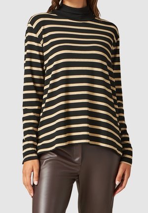 Woman wearing a black and beige horizontal striped long-sleeve top with a black turtleneck, paired with dark brown leather pants.