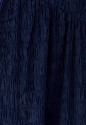Tmavě modrá texturovaná látka s vertikálními plizé, s klesajícími a hladkými sekcemi, vytvářející strukturovaný vzhled.