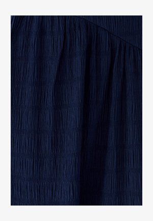 Tmavě modrá texturovaná látka s vertikálními plizé, s klesajícími a hladkými sekcemi, vytvářející strukturovaný vzhled.