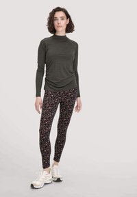 Donkergroene langemouwen top met geraapte zijkanten, gecombineerd met strakke legging met een luipaardprint in roze en zwart. Witte sneakers.