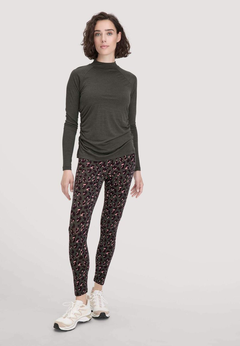 Donkergroene langemouwen top met geraapte zijkanten, gecombineerd met strakke legging met een luipaardprint in roze en zwart. Witte sneakers.