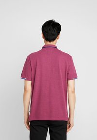 Kortärmad polotröja i melerad vinröd med marinblå krage, randiga ärmdekorationer och en avslappnad passform, tillverkad av andningsbart material.