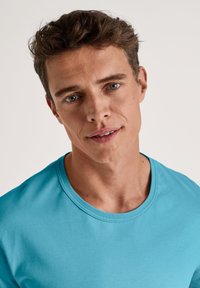 Turquoise crewneck t-shirt van glad katoen. Heeft korte mouwen en een fitted ontwerp. De stof heeft een lichte textuur.