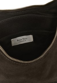 Vue intérieure d'un sac marron foncé avec fermeture éclair montrant une étiquette en tissu indiquant "PART TWO est. Copenhagen 1986."