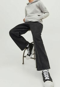 Svarta denimjeans med en avslappnad passform, i kombination med en ljusgrå huvtröja och svarta sneakers med vit sula och snörning.