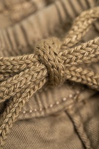 Beiger Baumwollstoff mit einer geflochtenen Zugkordel, die einen straffen Knoten aufweist. Die Textur ist glatt, mit versteckten Nähdetails entlang der Kanten.