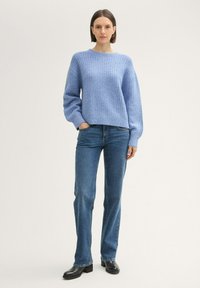 Hellblauer gestrickter Pullover mit strukturiertem Muster, lockerer Passform, überschnittene Schultern, kombiniert mit dunkelblauen geraden Jeans und schwarzen Stiefeln.