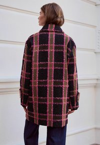 Karierte Wolljacke in Schwarz, Pink und Beige mit hohem Kragen, übergroßer Passform und geknöpften Manschetten, ausgestattet mit einem strukturierten Stoff und einem definierten Karomuster.