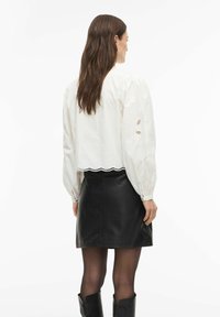 Balta krekla bl�ūze ar pūstām piedurknēm un mežģīņu detaļām aprocēs, kombinēta ar melnu ādas mini svārku un melniem zābakiem līdz ceļiem.