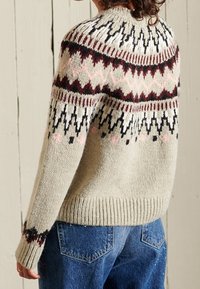 Neulepaita vaaleassa beigeissä, jossa on geometralinen kuvioväri mustana, viininpunaisena ja vaaleanpunaisena. Siinä on ribbineuleinen helma ja leveät hihat. Rennon mallinen.