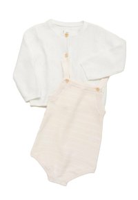 Cardigan alb tricotat cu două butoane din lemn, asortat cu un salopet de culoare bej deschis, cu dungi, care are butoane pe umăr și închidere cu capse.
