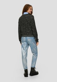 Zwarte gebreide trui met een cropped ontwerp, gecombineerd met lichtblauwe glanzende jeans en zwarte veterschoenen. Model van achteren getoond.