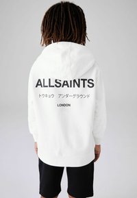 Fehér kapucnis felső, nagy fekete "ALLSAINTS" logóval a hátsó részen, amelyhez japán szöveg és "LONDON" is tartozik. Puha anyag, letisztult dizájn.