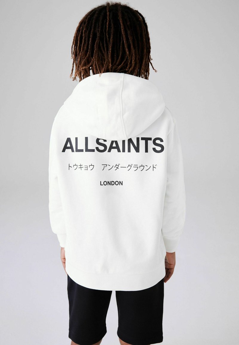 Fehér kapucnis felső, nagy fekete "ALLSAINTS" logóval a hátsó részen, amelyhez japán szöveg és "LONDON" is tartozik. Puha anyag, letisztult dizájn.