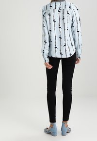 Ljusblå långärmad blus med svart fågeltryck, matchad med svarta skinny jeans och ljusblå klackskor med dekorationer.