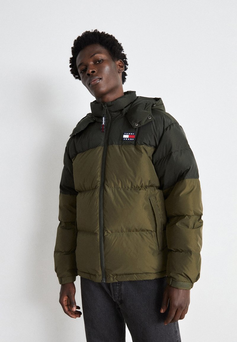 Chaqueta acolchada en verde y verde oscuro con cierre de cremallera, cuello alzado y parche de logo en el pecho; cuenta con bolsillos y capucha.