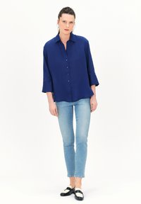 Navyblauw overhemd met knopen, een kraag, driekwartmouwen en een relaxte fit. Gecombineerd met lichtblauwe jeans en zwart-witte loafers.