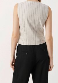 Hihaton pellavapusero vaaleanbeigessä, jossa pystysuorat tummansiniset raidat. Tiukan mallinen, sileä pinta, yhdistetty mustiin räätälöityihin housuihin, joissa on takataskut.