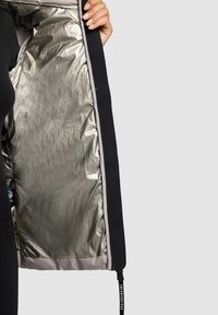 Sort jakke med en skinnende sølv indvendig foret, der har en lynlås og en sort træk-flig med hvid tekst. Glat ydre tekstur.