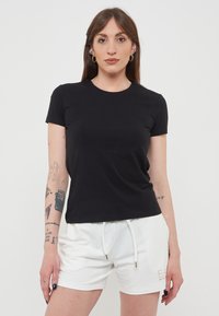 T-shirt nera a maniche corte con scollatura rotonda, realizzata in tessuto liscio. Abbinata a pantaloni corte bianchi con cordoncino e dettagli del logo.