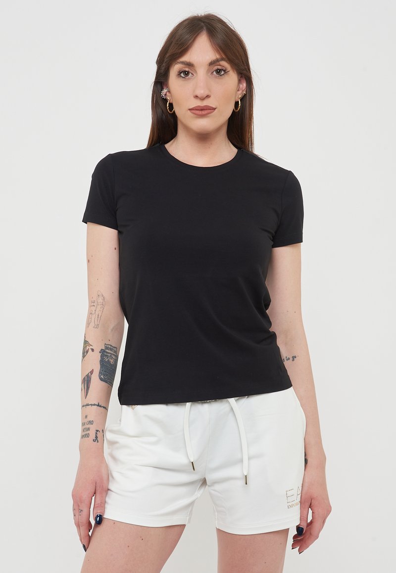 T-shirt nera a maniche corte con scollatura rotonda, realizzata in tessuto liscio. Abbinata a pantaloni corte bianchi con cordoncino e dettagli del logo.