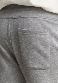Gros plan de la poche arrière d'un pantalon de survêtement gris avec des coutures visibles et une taille élastique sous un haut blanc.