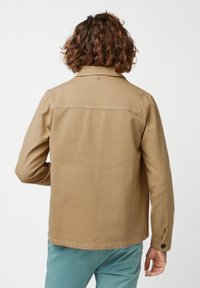 Beige katoenen jack met een knoopkraag, rechte zoom en knoopmanchetten, voorzien van een rugpas en een minimalistisch ontwerp.
