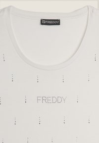 Maglietta bianca con scollatura rotonda, presenta strass argentati disposti in verticale e il nome del marchio "FREDDY" scritto con strass.