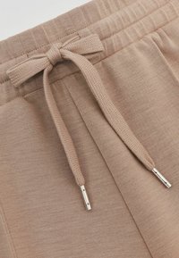 Beige sweatpants van een gestructureerde stof, met een trekkoord met metalen uiteinden en zijzakken. Glad, elastische tailleband.