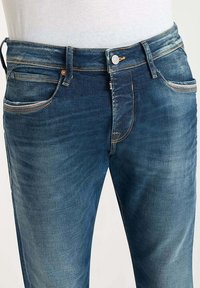 Vaqueros de mezclilla de color azul oscuro con corte recto, que cuentan con un cierre de botón, cinco bolsillos y costuras contrastantes a lo largo de las costuras.