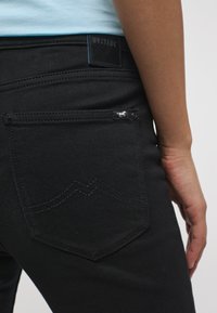 Juodos džinsus, pagamintus iš denimo, su užpakalinėmis kišenėmis su subtiliu siuvinėjimu ir mažais metaliniais akcentais. Oda ženklelis ant diržo.