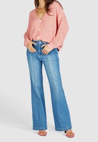 Rosa, stickad kofta med v-ringning och knäppning, tillsammans med ljusblå, utsvängda, högmidjade jeans med sidsömmar och fickor.